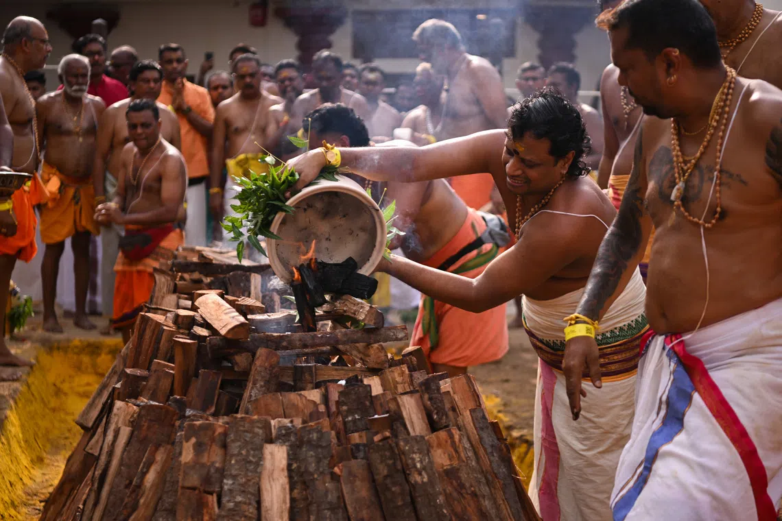 The head pandaram Venugopal Thirunavukarasu (second right) pouring fire coals into the firewood at 9am to ignite the fire pit.