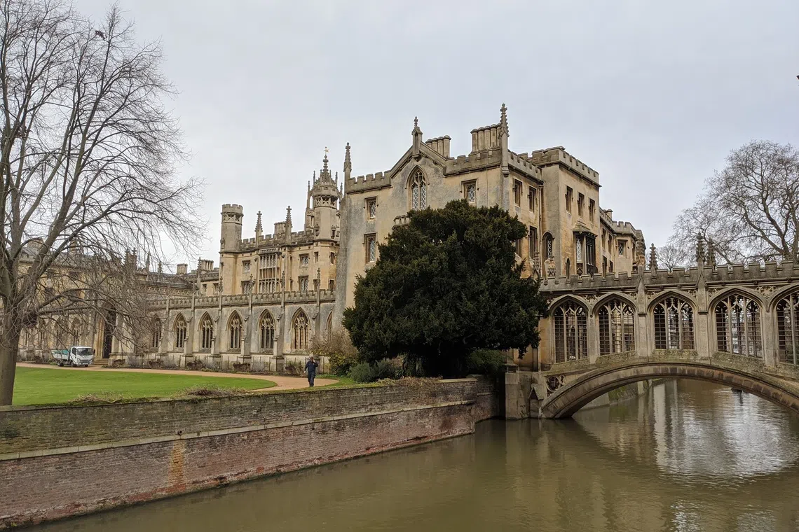 A large, historic stone building next to a river with a small bridge.
