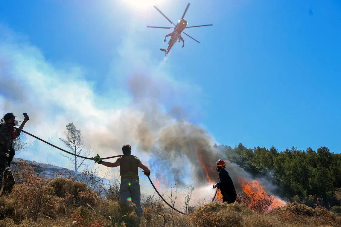 FILE PHOTO: A firefighting helicopter flies over a firefighter and volunteers trying to extinguish a wildfire burning in Keratea, near Athens, Greece, June 30, 2024. REUTERS/Elias Marcou/File Photo