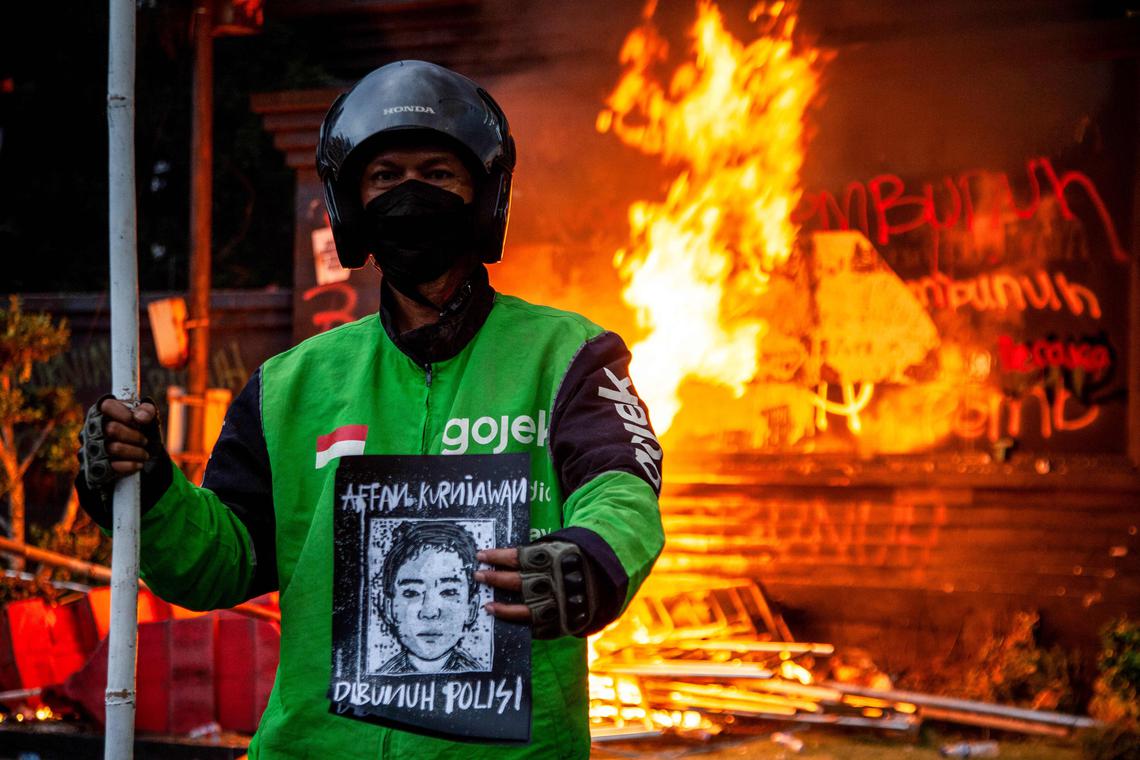 A man wearing a biker's jacket holds a portrait of the motorcycle taxi driver who was run over by an armoured Brimob (Mobile Brigade Corps) vehicle the night before, during a protest against police in front of the Greater Jakarta Metropolitan Regional Police headquarters in Jakarta on August 29, 2025. Protests erupted across several Indonesian cities on August 29 in anger at the death of a motorcycle taxi driver hit by a police vehicle, as officers responded with tear gas and the president called for calm. (Photo by Aditya IRAWAN / AFP)