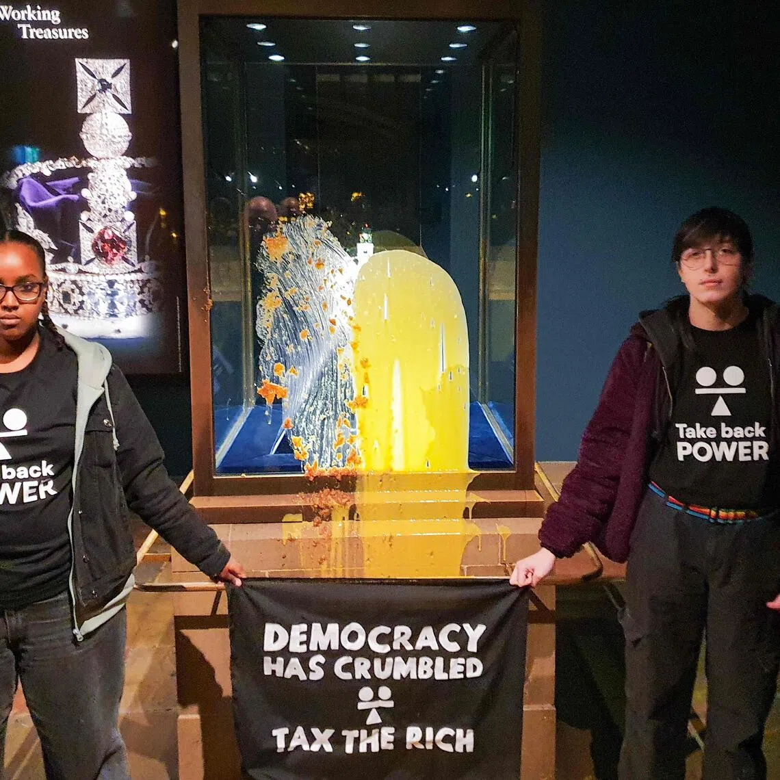 A handout photo by civil resistance group Take Back Power on Dec 6 shows supporters holding a banner after they smothered dessert and custard over the case containing the Crown Jewels at the Tower of London.