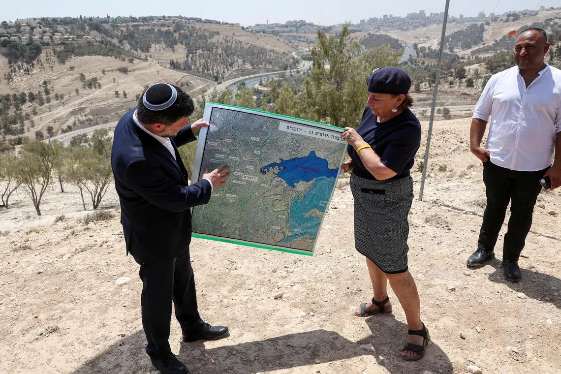 FILE PHOTO: Israeli Finance Minister Bezalel Smotrich and a woman hold a map that shows the long-frozen E1 settlement scheme, that would split East Jerusalem from the occupied West Bank, on the day of a press conference near the Israeli settlement of Maale Adumim, in the Israeli-occupied West Bank, August 14, 2025. REUTERS/Ronen Zvulun/File Photo