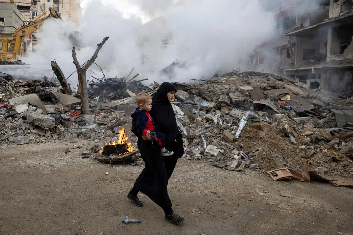 A woman carries her child as she walks past a destroyed building, after a ceasefire between Israel and Iran-backed group Hezbollah took effect at 0200 GMT on Wednesday after U.S. President Joe Biden said both sides accepted an agreement brokered by the United States and France, in Tyre, Lebanon, November 27, 2024. REUTERS/Adnan Abidi