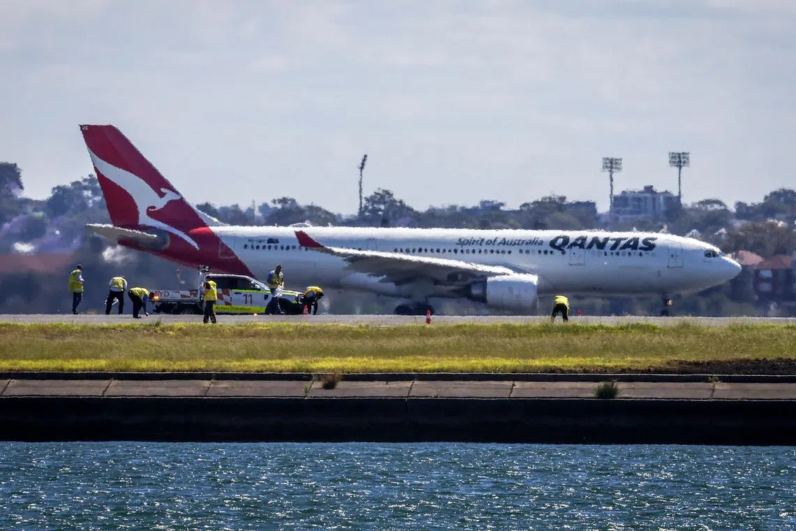 Workers check the runway as a Qantas plane prepares to take off behind them at Sydney International Airport on Nov 8, 2024. 