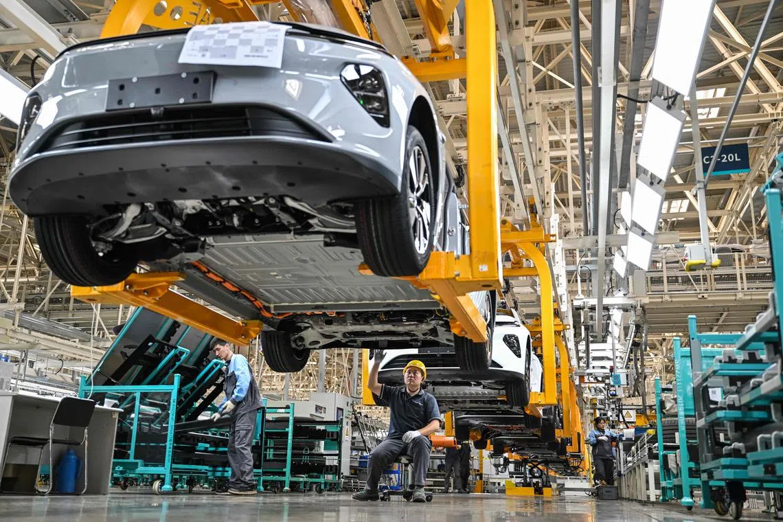 An employee (C) checks under a car along the assembly line at a factory of Chinese automaker NIO in Hefei, in China's eastern Anhui province on May 10, 2023. (Photo by HECTOR RETAMAL / AFP)