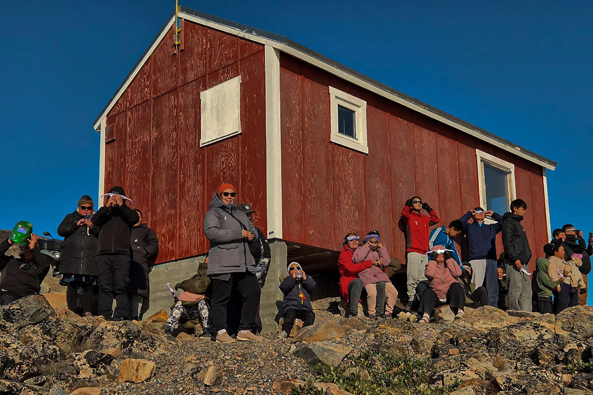 TOPSHOT - Inuit people look at the total eclipse on August 12, 2026 Ittoqqortoormiit, the only Eastern village in Greenland. The eclipse was mainland Europe's first total eclipse since 2006. Throughout human history eclipses have stirred amazement, fear and reverence, as they appear to momentarily halt the normal course of nature, creating a strange twilight during which temperatures drop, shadows appear at strange angles and some animals go to sleep. (Photo by Charlotte Pike / AFP)