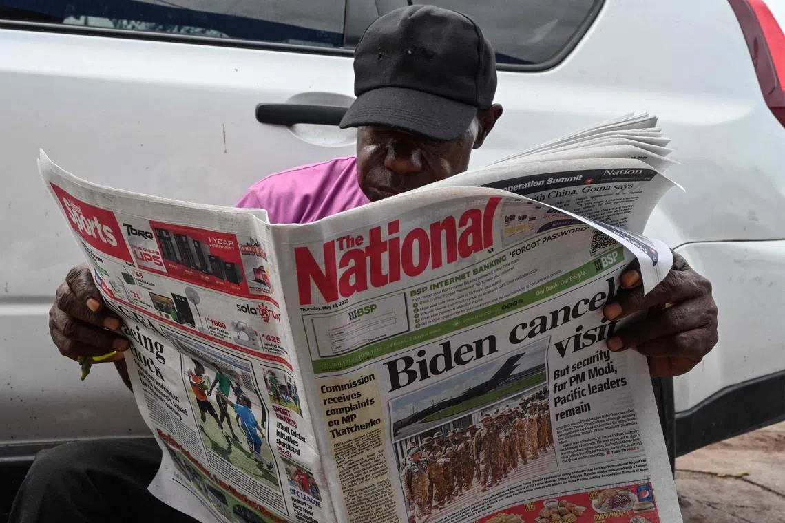 A man in Port Moresby reading a newspaper reporting on the cancellation of a visit to Papua New Guinea by US President Joe Biden.