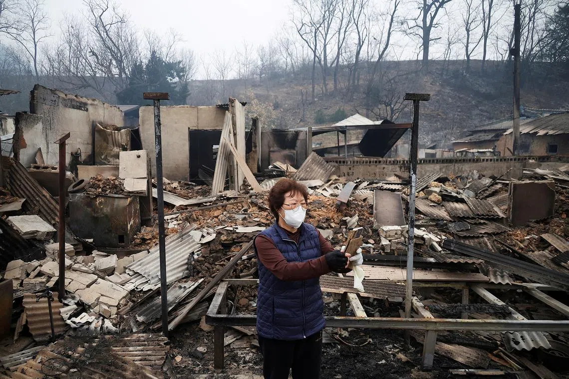 Kun Yeong-nam, 72, uses her mobile phone near her burnt house, where she lived for 52 years, after a wildfire devastated the area in Uiseong, South Korea, on March 27, 2025.