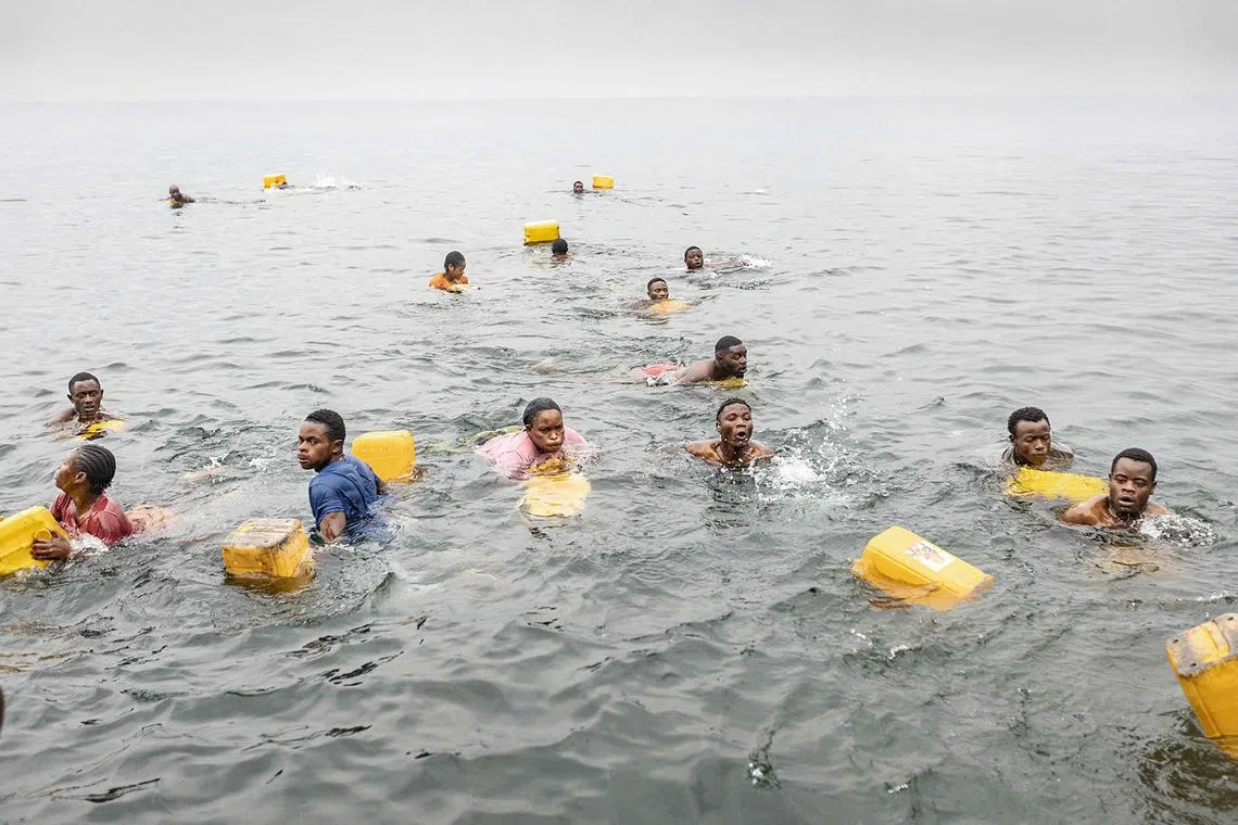 TOPSHOT - Residents swim while carrying their jerrycans as they gather to collect water amid ongoing water shortages at the shore of Lake Kivu in Goma on January 29, 2025. Rwanda-backed fighters controlled almost all of the DR Congo city of Goma on January 29, 2025 where residents were re-emerging after days of deadly fighting and Angola urged leaders of both countries to urgently hold peace talks. After intense fighting that saw the M23 armed group and Rwandan troops seize the city's airport and key sites, calm returned to the mineral trading hub. (Photo by AFP)