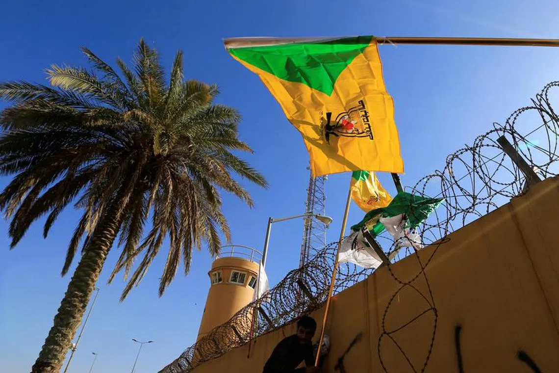 FILE PHOTO: A member of Hashd al-Shaabi (paramilitary forces) holds a flag of Kataib Hezbollah militia group during a protest to condemn air strikes on their bases, outside the main gate of the U.S. Embassy in Baghdad, Iraq December 31, 2019. REUTERS/Thaier al-Sudani
