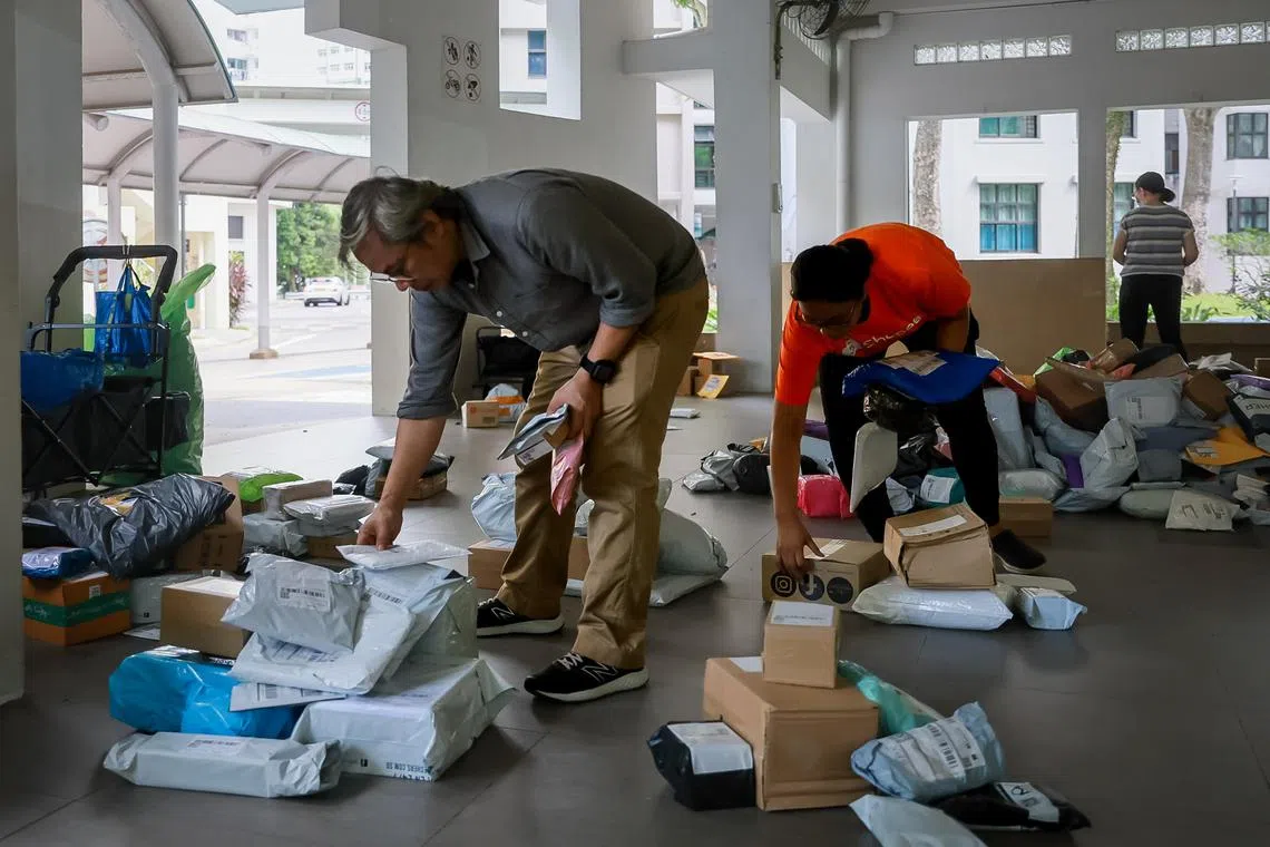 The Straits Times Senior Correspondent John Lui sorting the parcels according to their addresses at a multipurpose hall in Senja, Sep 13, 2023. With him is Suriati binte Abdullah Sani and her husband Aziz bin Basiron. The couple is in charge of delivering the parcels to a few blocks in Senja.