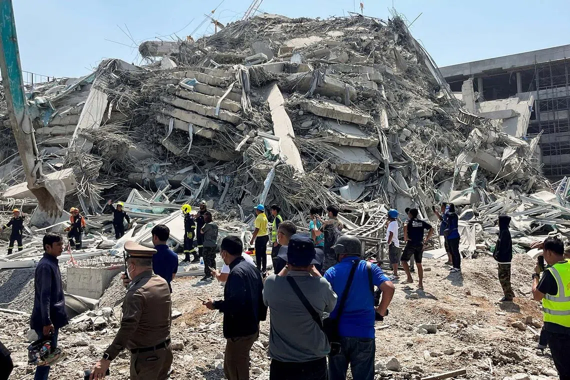 People standing near the site of a collapsed building in Bangkok after a strong earthquake struck central Myanmar on March 28, 2025, with hundreds of people pouring out of buildings in the Thai capital in panic.