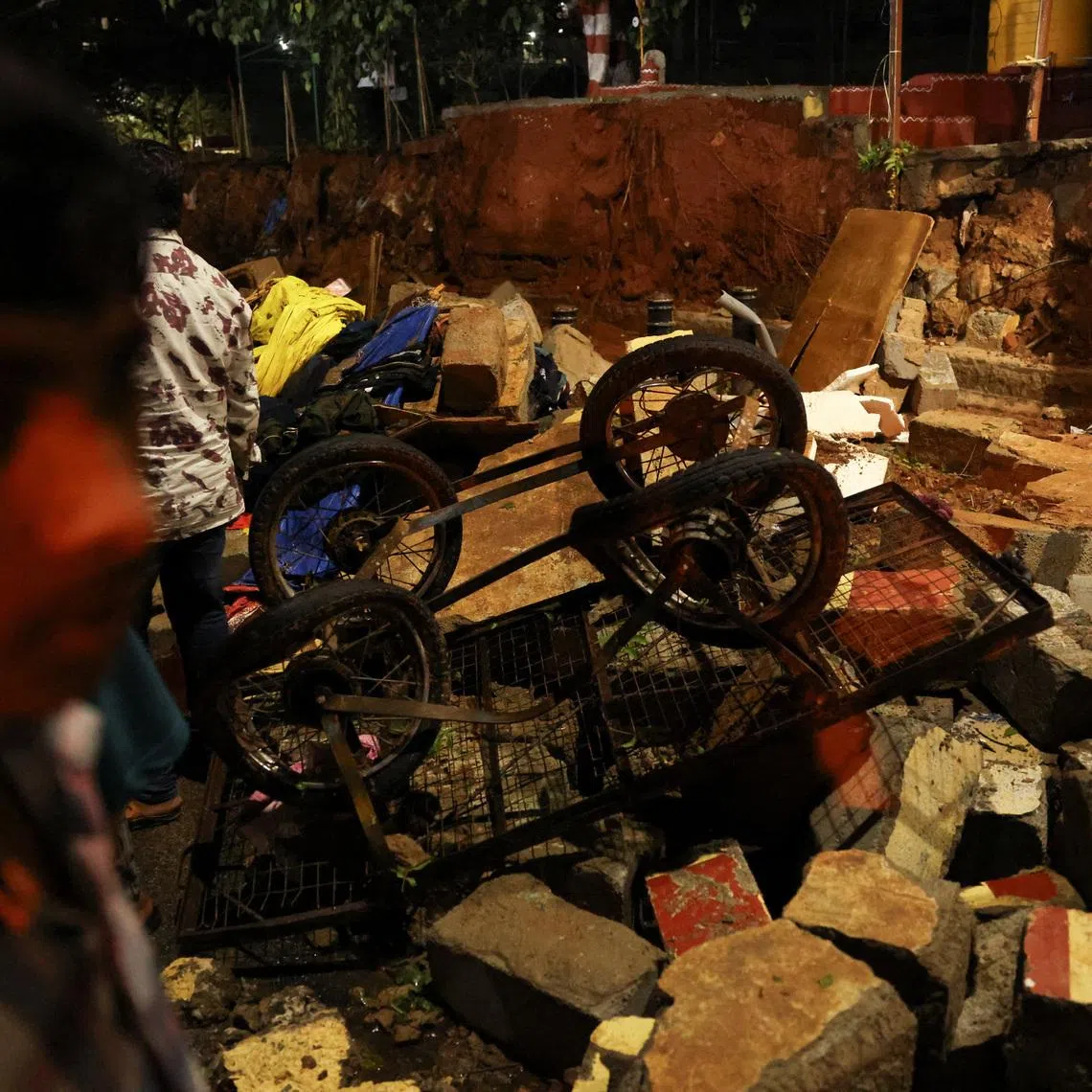 People standing next to debris from a collapsed compound wall of a hospital following rains in Bengaluru, India, April 29, 2026.