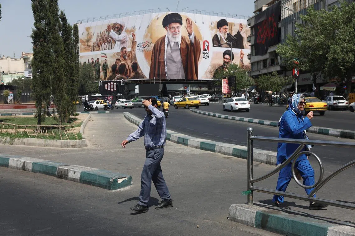People walk past a billboard featuring images of Iran’s late Supreme Leader Ali Khamenei in Tehran on July 13.