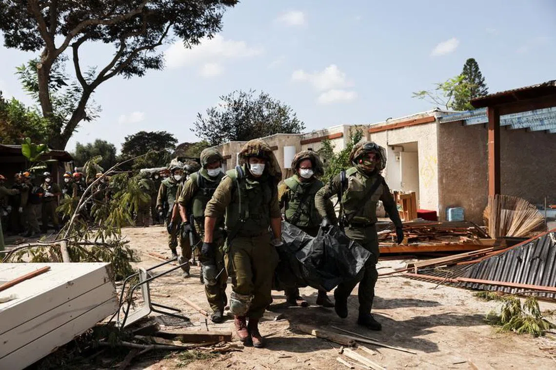 Israeli soldiers carry the body of a victim of an attack by militants from Gaza at Kibbutz Kfar Aza, in southern Israel, October 10, 2023. REUTERS/Violeta Santos Moura