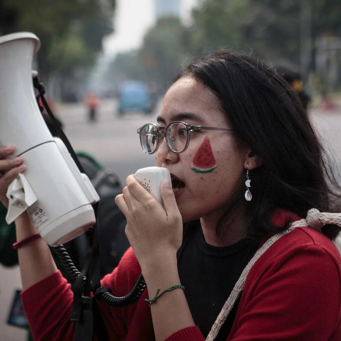 A woman with a watermelon face paint shouts slogans into a megaphone during a protest in solidality with the Palestinian people in front of the US embassy in Jakarta on November 9, 2023. Thousands of civilians, both Palestinians and Israelis, have died since October 7, 2023, after Palestinian Hamas militants based in the Gaza Strip entered southern Israel in an unprecedented attack triggering a war declared by Israel on Hamas with retaliatory bombings on Gaza. (Photo by ADITYA AJI / AFP)