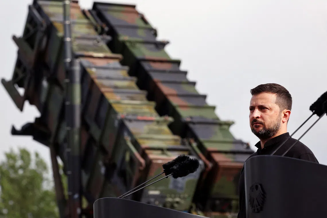 A man speaking at a podium with a military vehicle behind him.