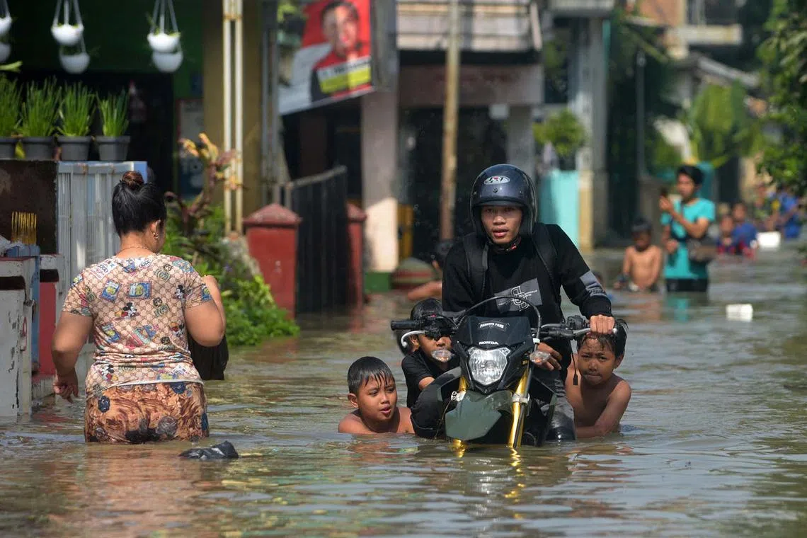 Children help push a motorcycle through a waterlogged road during flooding at Bojongasih village, in Bandung, West Java on November 21, 2024, caused by a river overflowing after heavy rain, which resulted in hundreds of homes being submerged. (Photo by TIMUR MATAHARI / AFP)
