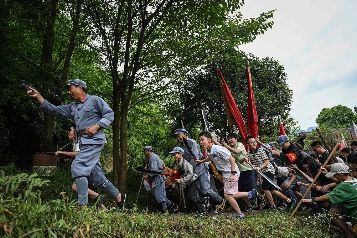 TOPSHOT - This photo taken on July 25, 2026 shows performers in Red Army uniforms and tourists participating in a reenactment of a battle between Chinese Communist and Nationalist forces, at Loushan Pass in Zunyi, in southwestern China's Guizhou Province. Dressed in Red Army uniforms and waving prop weapons, scores of tourists stormed a mound in southwestern China's Loushan Pass as flashy explosions light up the hillside in a reenactment of a historic battle. (Photo by Jade GAO / AFP) / To go with 'China-Tourism-Culture' Visual story by Agatha CANTRILL