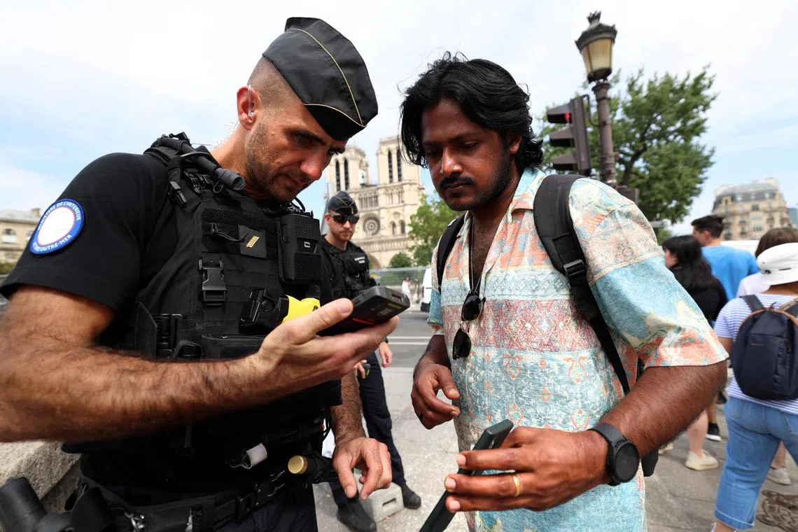 A French Gendarme inspecting the QR code of a pedestrian on their smartphone, at the entrance to the "grey zone", a secure area set up across the River Seine in Paris, on July 18.