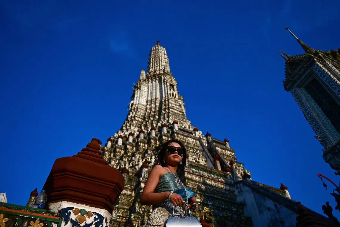 A tourist from China, dressed in a rented traditional Thai costume poses for photographs at the Wat Arun Buddhist temple in Bangkok on February 12, 2023. (Photo by Manan VATSYAYANA / AFP)