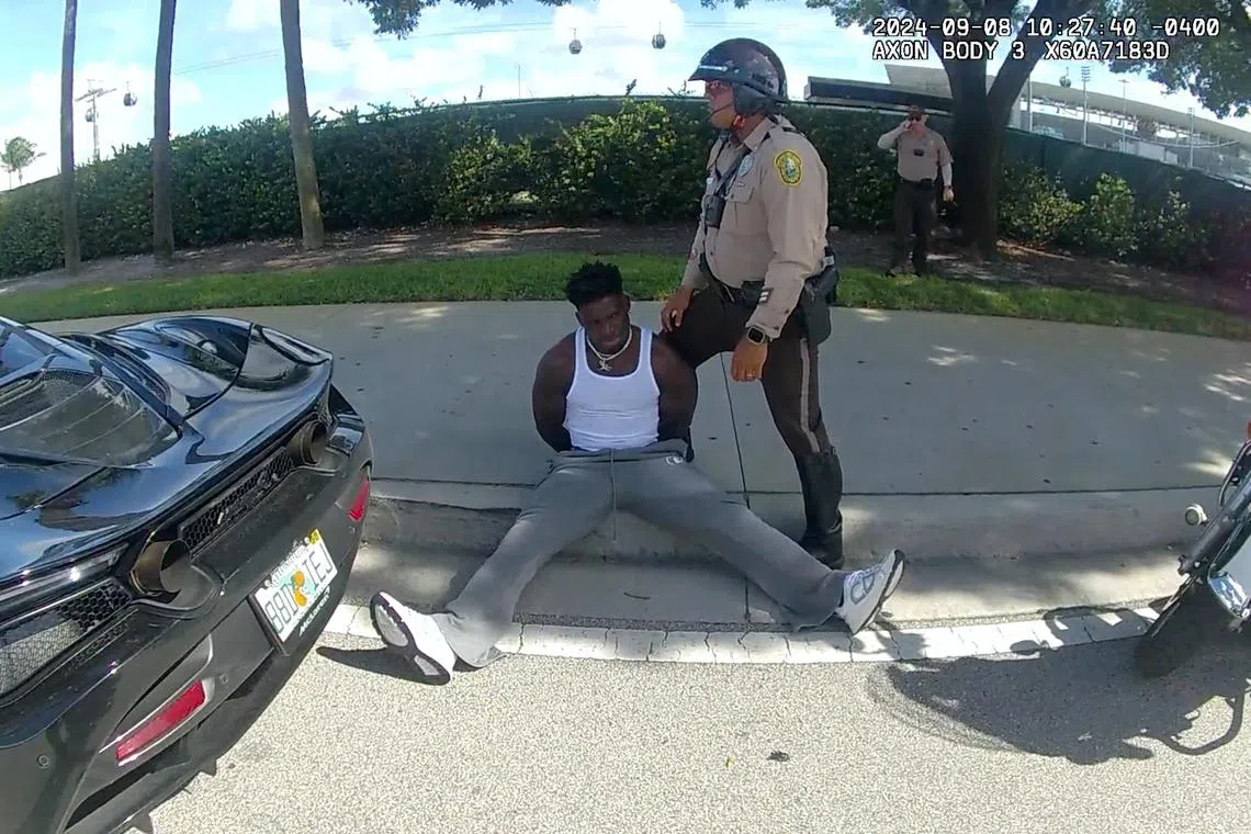 Miami Dolphins receiver Tyreek Hill sits handcuffed on the sidewalk during a traffic stop, in Miami Gardens, Florida.