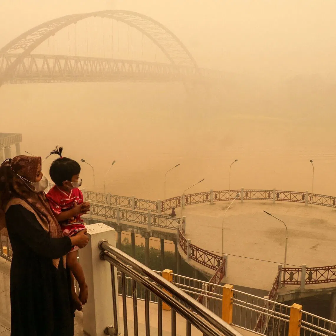 TOPSHOT - A child and mother wearing face masks look on from a bridge amid thick haze from forest and land fires in the region in Palangkaraya, Central Kalimantan, on October 12, 2026. Toxic haze has shrouded parts of Indonesia, Malaysia and Singapore for weeks as Jakarta struggles to contain fires that have scorched large tracts of Borneo and Sumatra, with the smoke drifting across the region. (Photo by REINA / AFP)