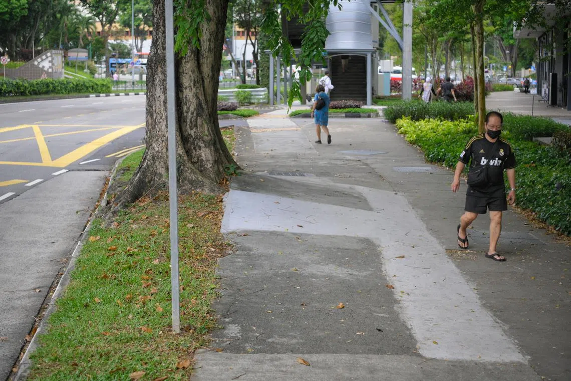 People walk along an uneven and damaged pavement along Jalan Bukit Merah on April 24, 2023.
