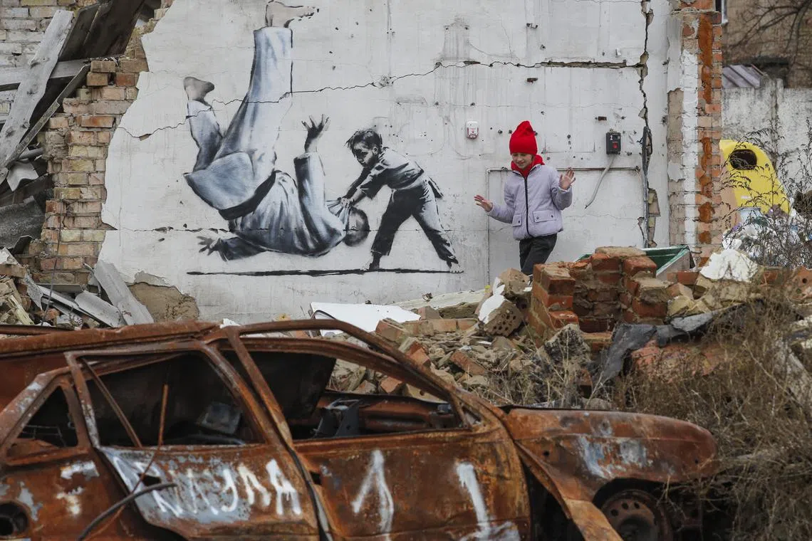 People watch a mural depicting child overthrowing a man in judo clothes, in a style resembling the works of British street artist Banksy, at a wall of a building that was destroyed during shelling in Borodyanka, Ukraine, 13 November 2022. A photo of a mural in Borodyanka depicting a gymnast was shared by Banksy on his social media channel on 11 November, while other works attributed to him in different locations in Ukraine and resembling Banksy's style have not been shared on the artist's channel yet. Russian troops entered Ukraine on 24 February 2022, starting a conflict that has provoked destruction and a humanitarian crisis.