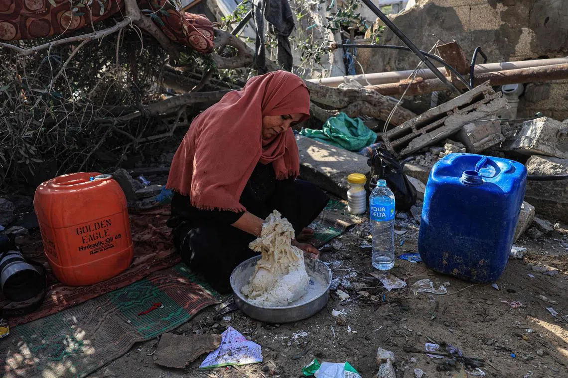 A woman mixes flour with water to make bread amid the ruins of the family home destroyed in an Israeli strike in Rafah in the southern Gaza Strip.