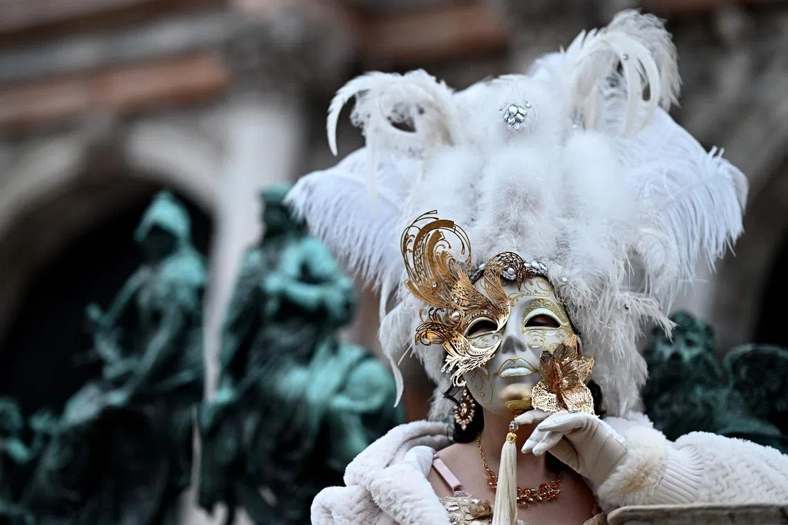A masked reveller wearing a period costume posing next to the Ponte dei Sospiri (Bridge of Sighs) during the pre-opening of the carnival in Venice on Jan 27, 2024. 
