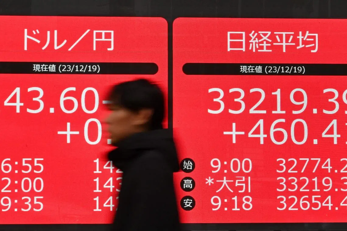 A pedestrian walks past an electronic board showing the rate of the Japanese yen versus the US dollar (L) and the closing numbers of the Tokyo Stock Exchange (R) along a street in Tokyo on December 19, 2023. (Photo by Kazuhiro NOGI / AFP)