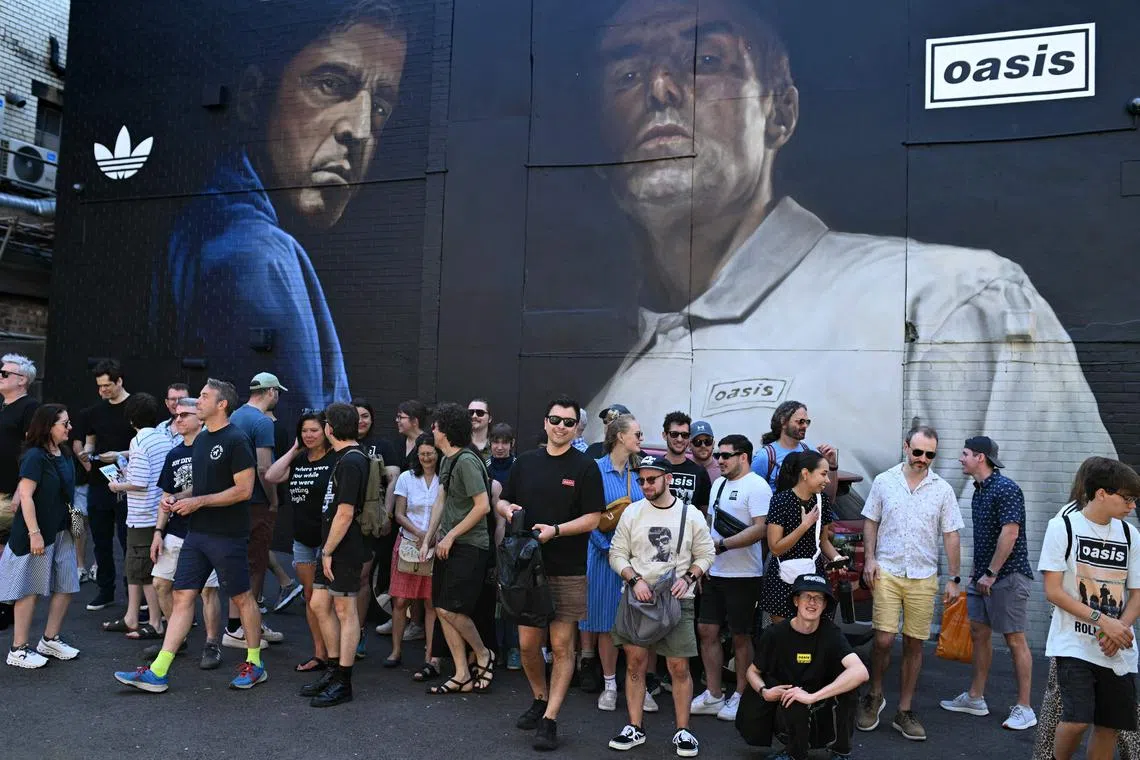 People pose in front of a mural of British rock band Oasis, in Manchester, northern England on July 11.