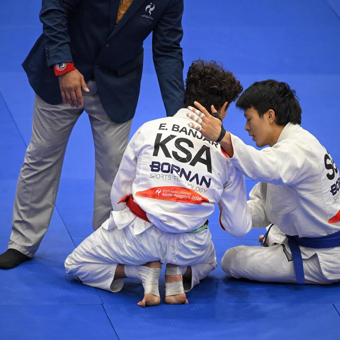Singaporean jiu-jitsu fighter Noah Lim (right) sitting down and putting a consoling arm around his defeated and emotional rival Elyas Zwawi Y Banjar of Saudi Arabia at the Asian Games.