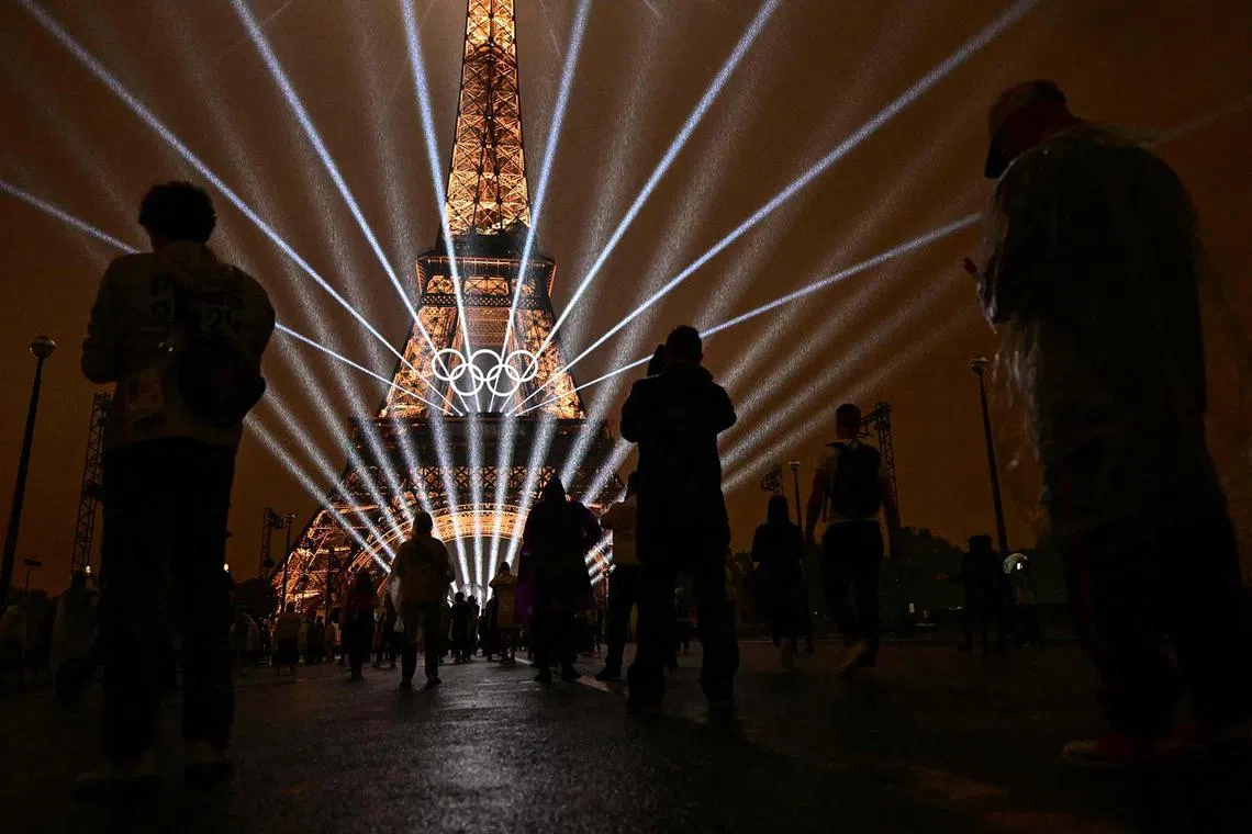 Attendees taking pictures of the Eiffel Tower as lasers light up the sky during the opening ceremony of the Olympic Games in Paris on July 26, 2024.
