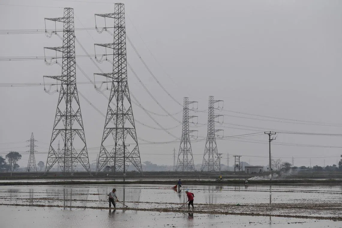 (FILES) Farmers work in a paddy field next to large electricity pylons on the outskirts of Hanoi on February 15, 2022. A severe power shortage in Vietnam caused by an intensely hot spell and unprecedented drought in May and June cost the country $1.4 billion, the World Bank said. (Photo by Nhac NGUYEN / AFP)