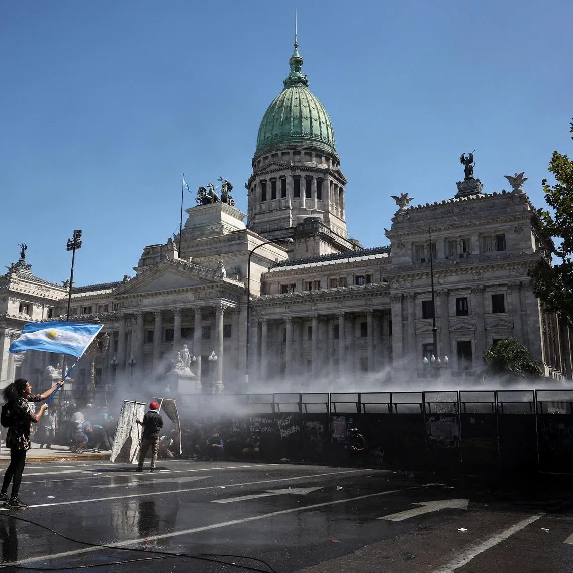 A demonstrator holds a flag as police use a water cannon during a protest outside Argentina's National Congress on the day senators vote on a labor reform law proposed by President Javier Milei's libertarian government to attract investment and revive growth, and which unions say will roll back workers' rights, in Buenos Aires, Argentina February 27, 2026. REUTERS/Agustin Marcarian