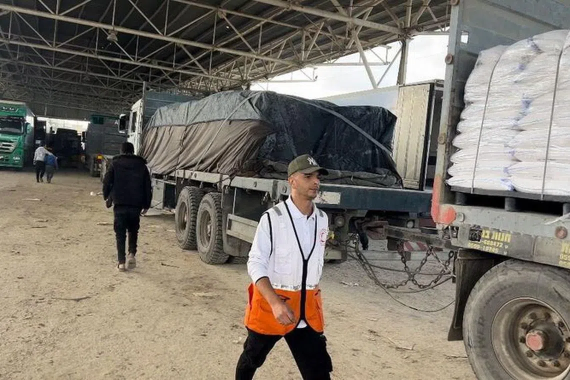 People walk next to trucks with humanitarian aid which entered Gaza through the Rafah border crossing between Egypt and the Gaza Strip, in this handout picture released on December 2, 2023.    Palestine Red Crescent Society/Handout via REUTERS