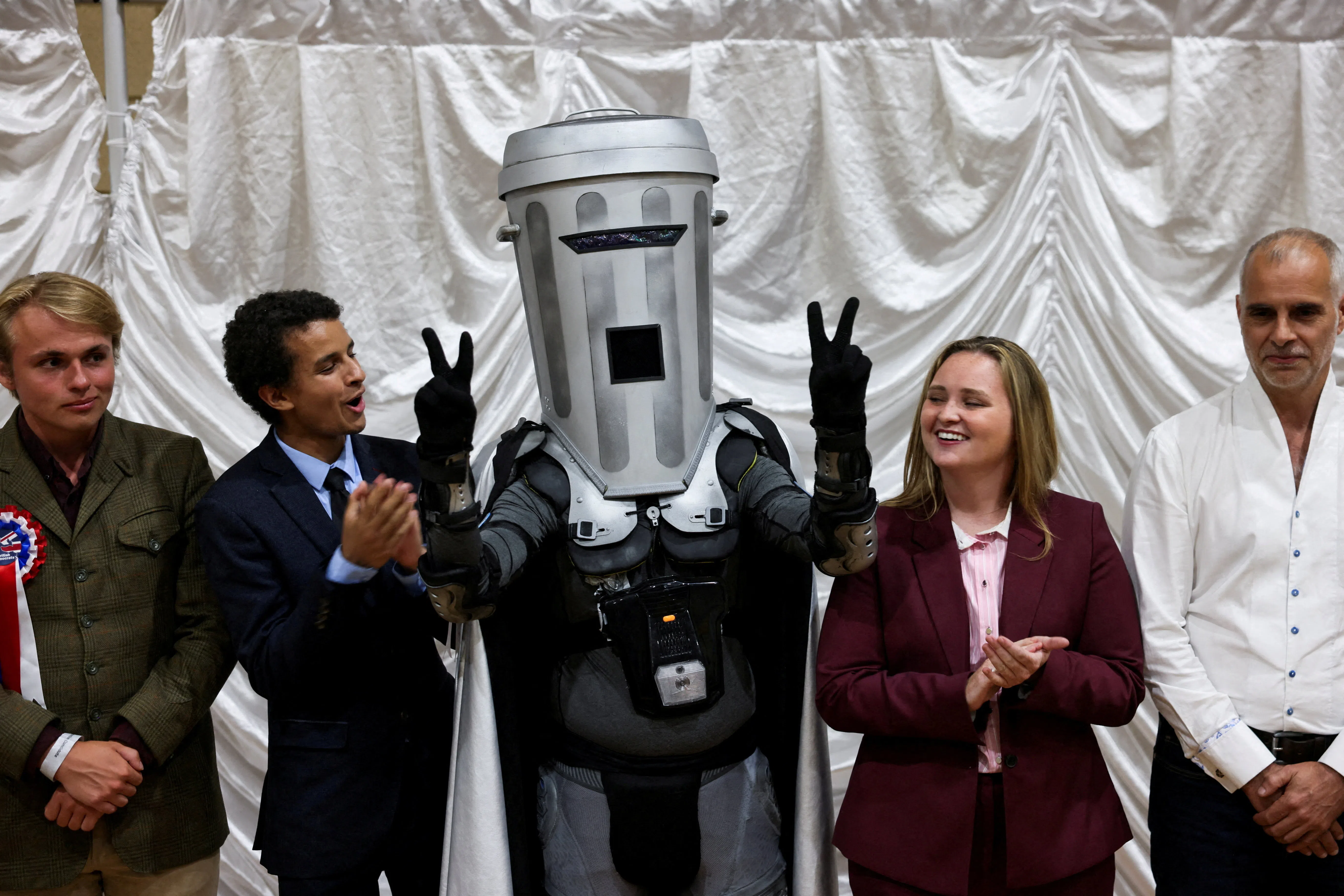 Count Binface gestures while standing with other candidates after Reform UK party leader Nigel Farage was declared the winner for the Clacton by-election, triggered by the resignation of Farage, in Essex, Britain, August 14, 2026. REUTERS/Jack Taylor     TPX IMAGES OF THE DAY       REFILE - UPDATING GRAMMAR