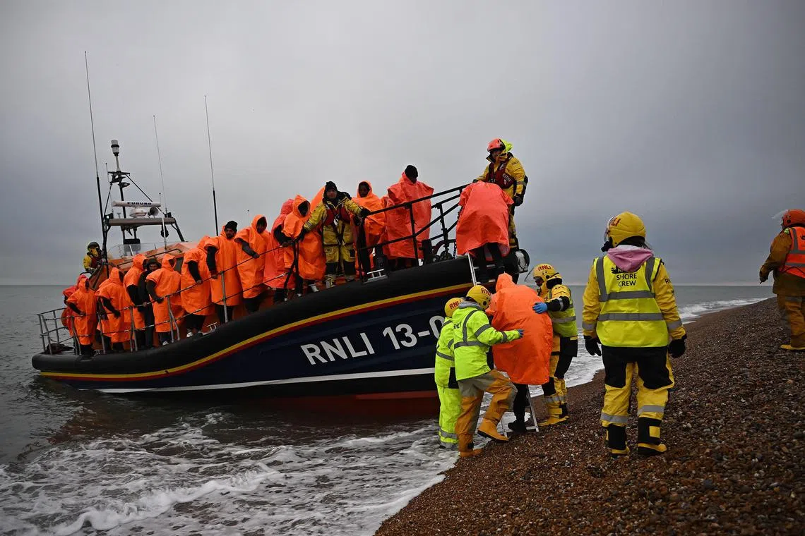 (FILES) In this file photo taken on December 9, 2022 migrants, picked up at sea attempting to cross the English Channel, are helped ashore from an Royal National Lifeboat Institution (RNLI) lifeboat, at Dungeness on the southeast coast of England. - UK high court judges ruled, on December 19, 2022 that the British government's controversial plan to deport migrants to Rwanda is lawful, after flights were thwarted through legal challenges by charities and asylum-seekers. In a bid to deal with the unprecedented number of arrivals, UK Prime Minister Rishi Sunak has sought to continue his predecessor Boris Johnson's scheme to deport migrants thousands of miles away to the African country. (Photo by Ben Stansall / AFP)
