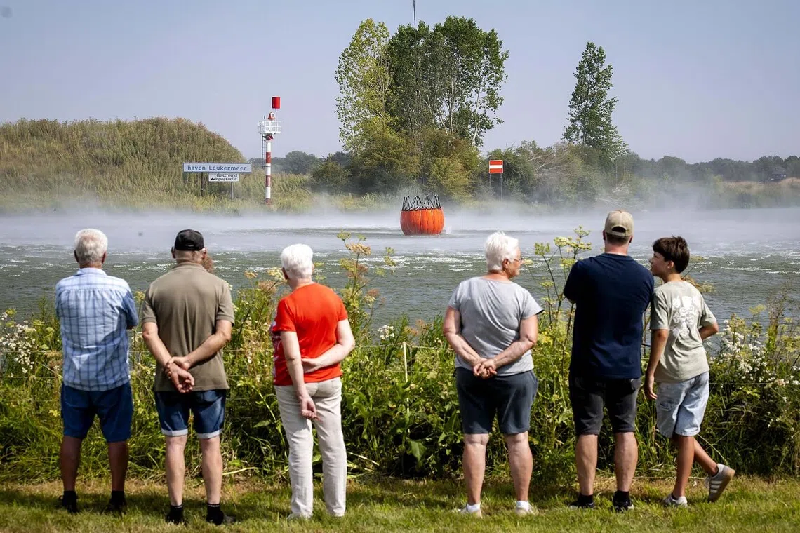 epa13149535 Day-trippers watch as a water bucket suspended beneath a Chinook helicopter is filled from the Meuse River in the Netherlands, 04 August 2026, during firefighting operations to combat a wildfire in the Boschhuizerbergen nature reserve. Multiple Defense firefighting helicopters have been deployed to battle the blaze, which has affected about 100 hectares of the nature reserve. EPA/SEM VAN DER WAL