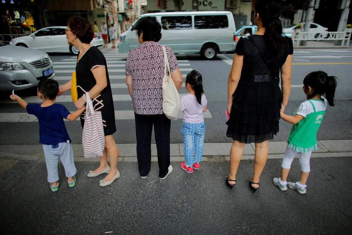 Women hold childrens' hands as they wait to cross a street after school in downtown Shanghai, China September 12, 2014.