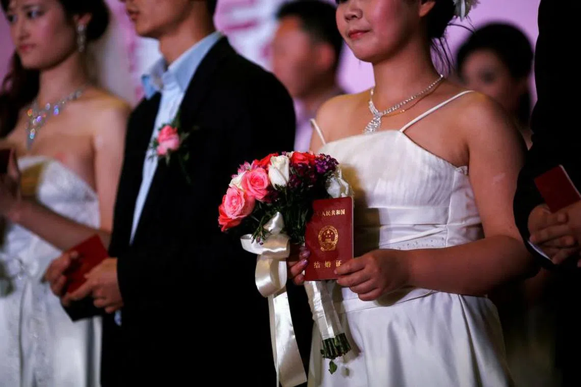 FILE PHOTO: A woman holds her marriage certificate as couples participate in a staged mass wedding, organised as part of a matchmaking event to inspire singles to get married, in a suburban area of Shanghai May 18, 2013. REUTERS/Carlos Barria/File Photo