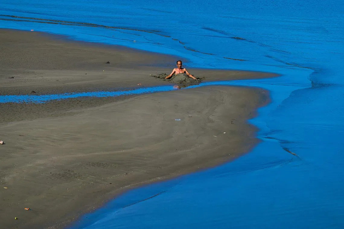 A man covers himself in beach sand as therapy in Banda Aceh on November 30, 2022.