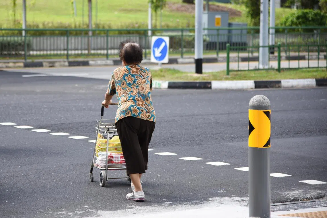 An elderly lady crossing a road with a shopping trolley at Tampines Avenue 4 on 20 February 2024.  elderly, seniors, mobility, ageing population, road safety