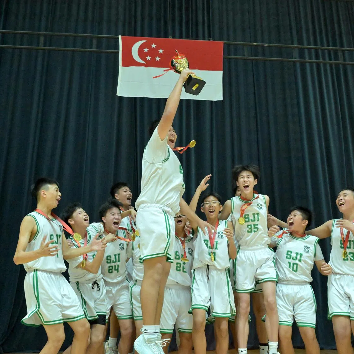 St Joseph's Institution captain Jude Ng hoists the C Division boys' basketball trophy as his team celebrates a 57-47 win over Presbyterian High School in the final.