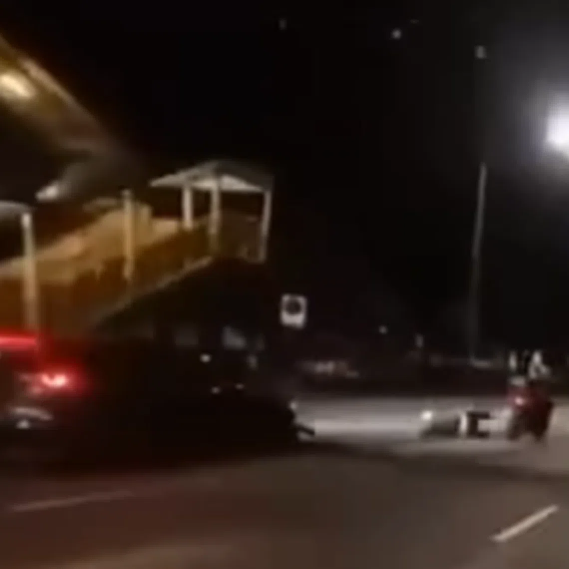 The car collides with the rear of a motorcycle in the left-most lane and the rider is flung off his bike before landing on the road.