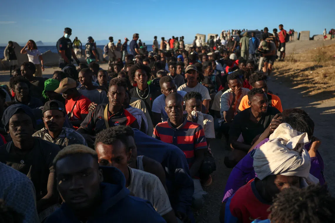 A large group of people sitting and standing on a dirt path near the ocean.