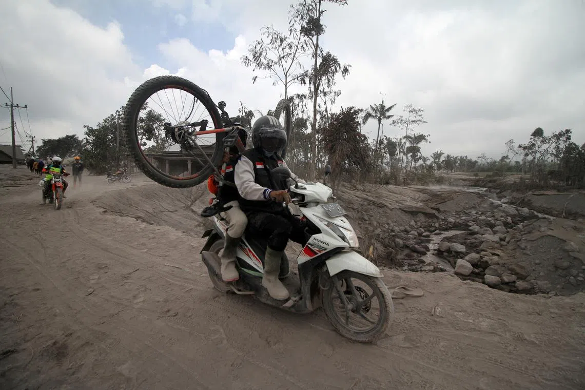 Volunteers ride on a motorbike as they move villagers' belongings out from an area affected by the eruption of Mount Semeru volcano in Sumberwuluh, Lumajang, East Java province, Indonesia, Dec 5, 2022, in this photo taken by Antara Foto. 