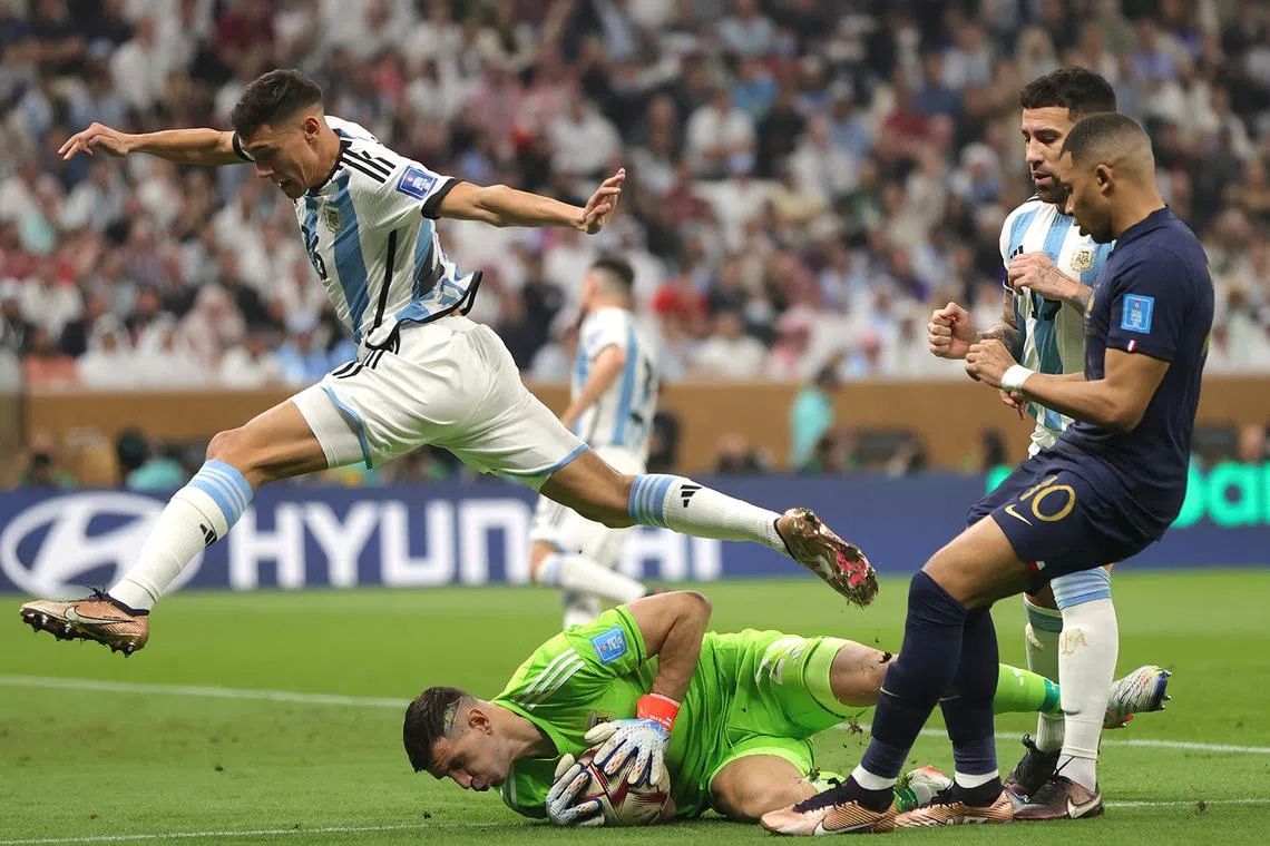Goalkeeper Damian Martinez (below) of Argentina saves the ball next to Kylian Mbappe (right) of France.